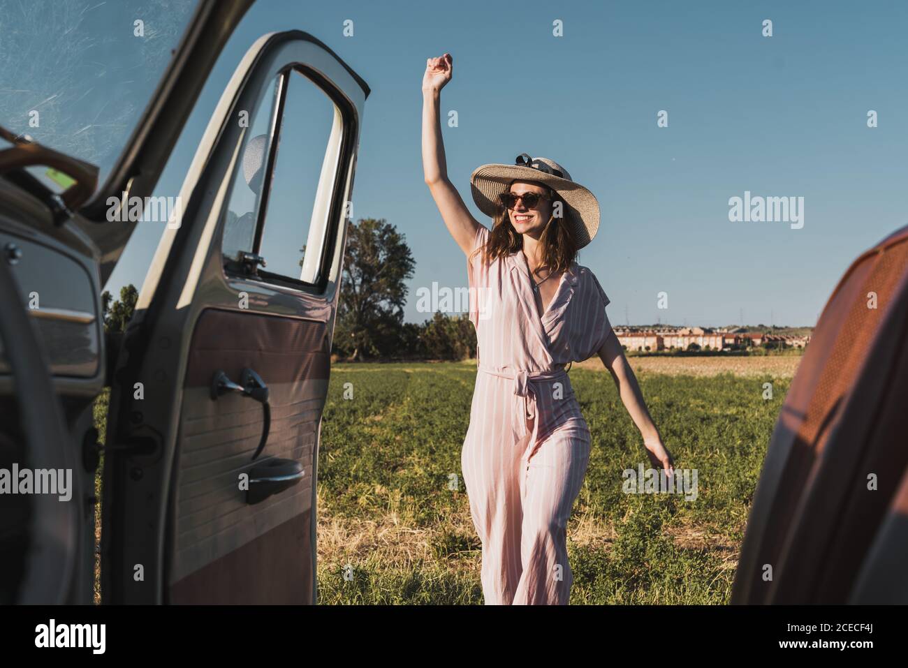 Vue de l'intérieur de la voiture rétro de la bonne femme à la mode dans le chapeau et les lunettes de soleil debout avec enthousiasme dans la nature et rire Banque D'Images