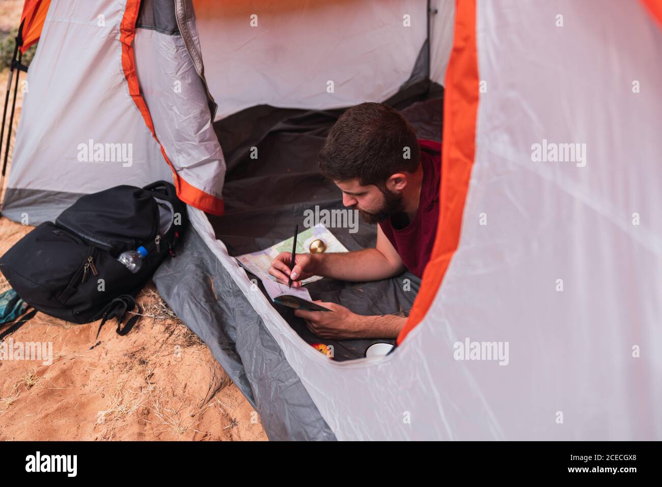 D'en haut de la photo d'un jeune homme allongé dans une tente et dessiner dans un carnet d'esquisses tout en campant dans le désert Banque D'Images