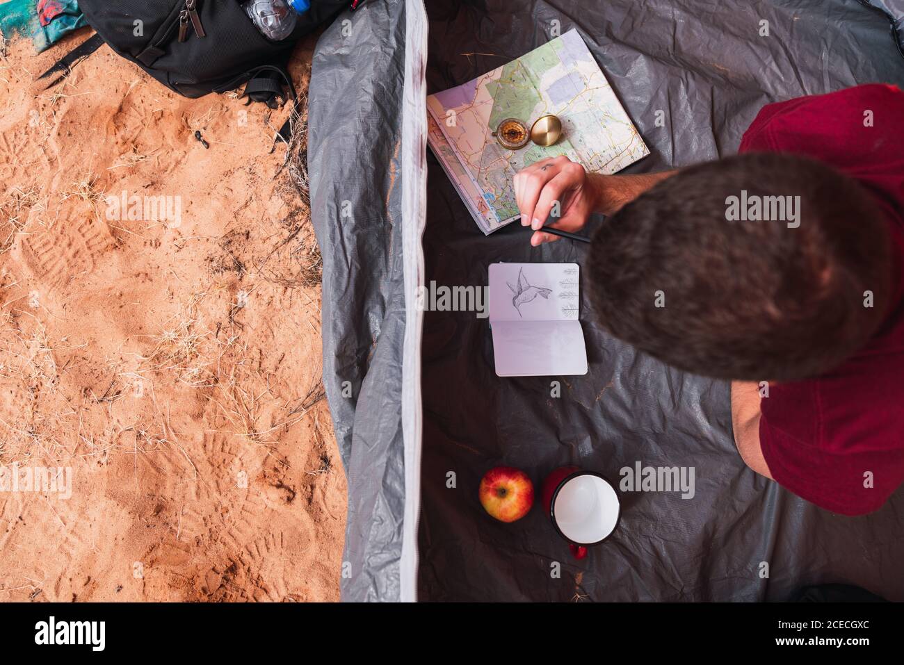 D'en haut de la photo d'un jeune homme allongé dans une tente et dessiner dans un carnet d'esquisses tout en campant dans le désert Banque D'Images