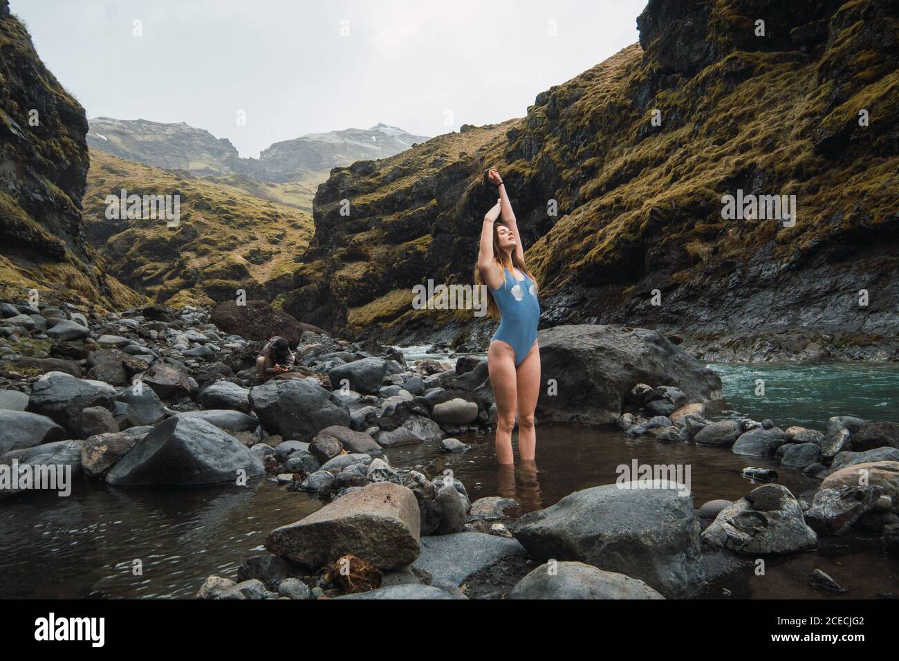 Jeune belle femme debout dans un maillot de bain dans la rivière de montagne avec de gros rochers avec les mains en haut Banque D'Images