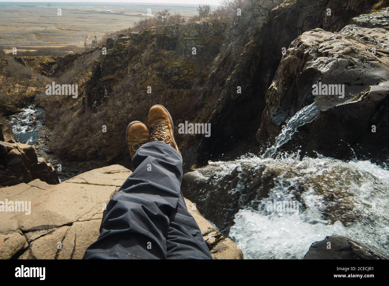 Crop jambes de l'homme assis sur le dessus de la montagne près chute d'eau en vêtements d'hiver Banque D'Images