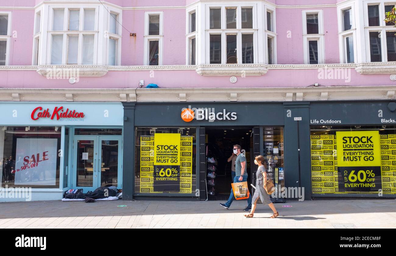Homme sans domicile dormant à l'entrée de la boutique fermée Cath Kidston Juste à côté de la boutique en plein air de Blacks qui a un stock Vente en liquidation à North Street Brighton Banque D'Images