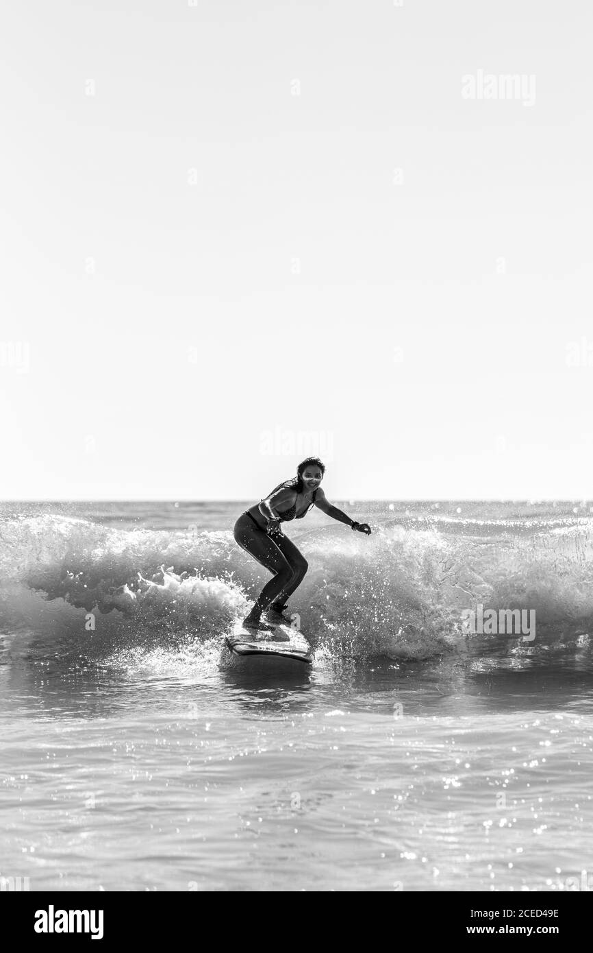 Photo en niveaux de gris d'une jeune femme surfant sur les vagues de la mer à Cadix, Espagne Banque D'Images