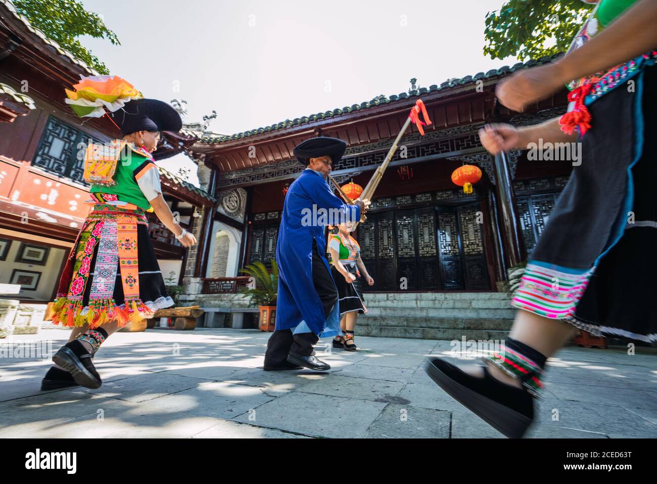 GUINZHOU, CHINE - 14 JUIN 2018: Miao groupe ethnique homme en vêtements bleus jouant des instruments de musique traditionnels et des femmes en costumes locaux lumineux dansant autour de lui pendant le festival dans le village de la province de Guizhou en Chine Banque D'Images