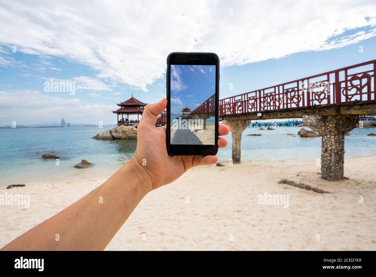 Rognez la main à l'aide d'un smartphone et prenez des photos de la passerelle sur la côte tropicale de l'île de Wuzhizhou, Hainan, Chine Banque D'Images