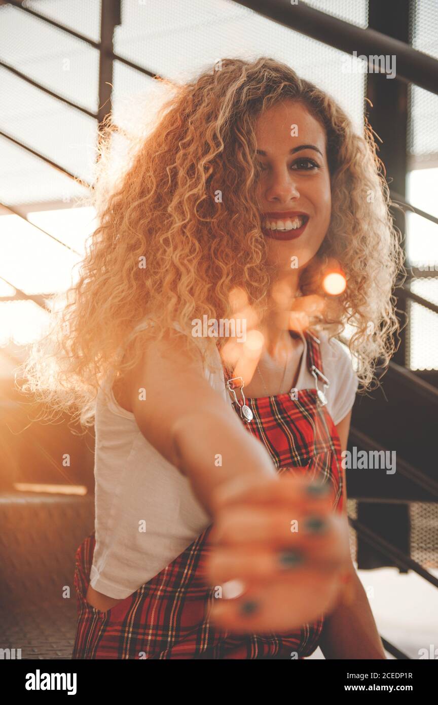 Merveilleuse jeune femme maussade souriant à la caméra tout en montrant un bâton lumineux flou assis dans les escaliers au soleil Banque D'Images