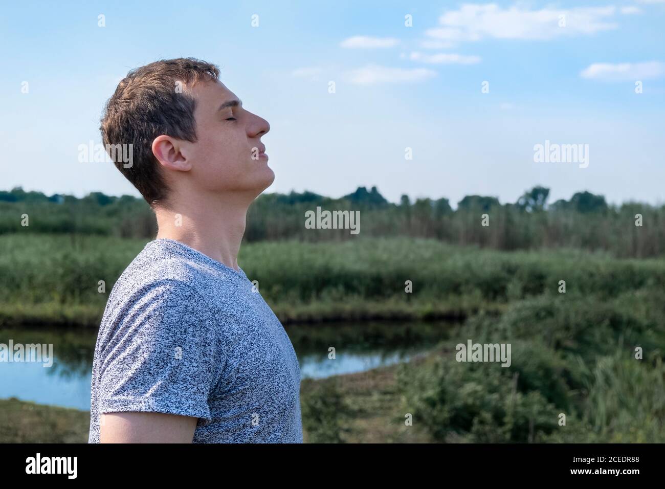 Homme adulte détendu respirant de l'air frais à l'extérieur avec le lac et champ en arrière-plan Banque D'Images