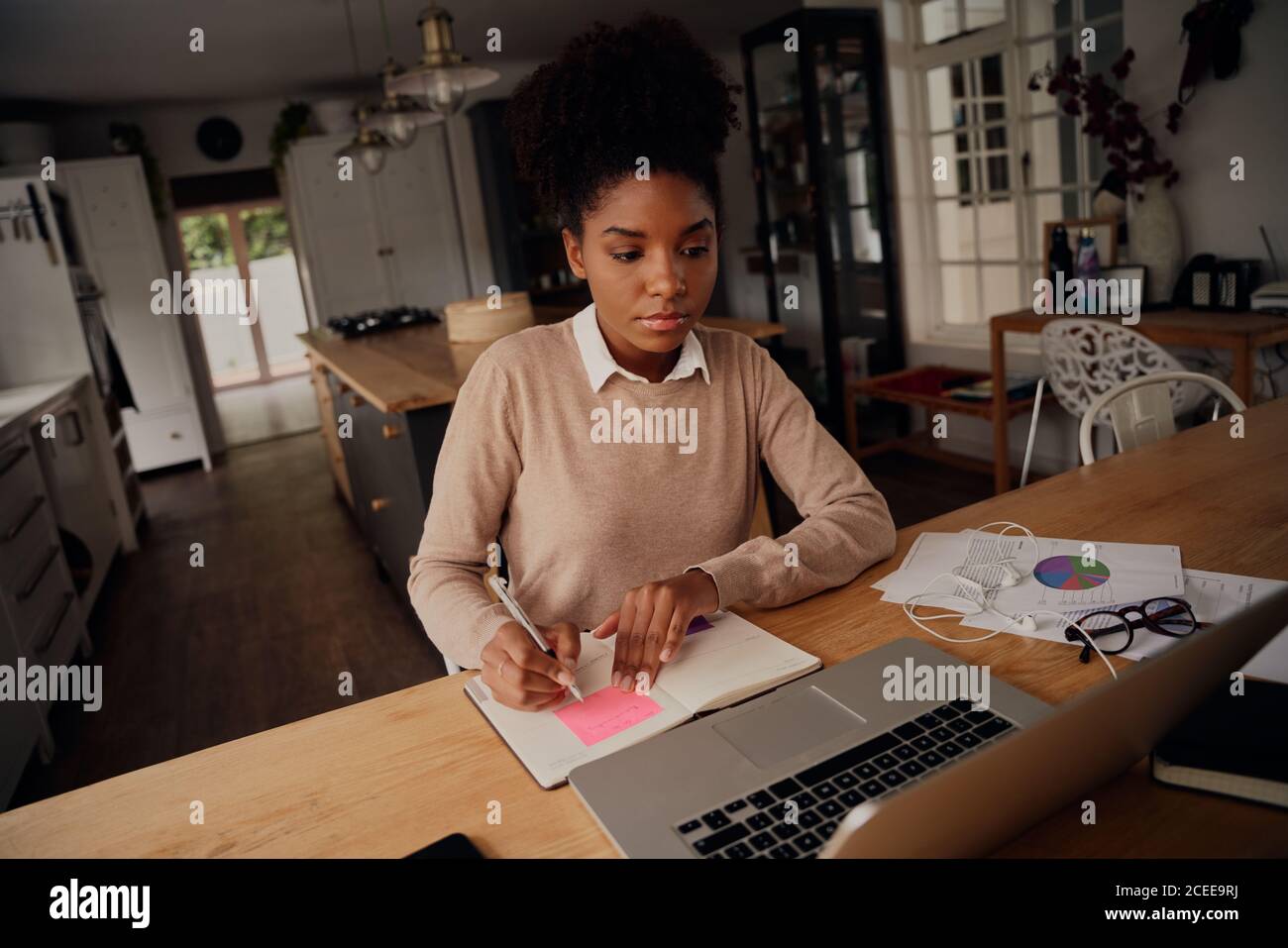 Jeune freelance écrivant des détails sur le livre tout en travaillant sur ordinateur portable à la maison pendant le maintien Banque D'Images