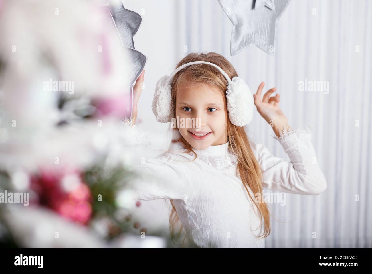 Belle petite fille en casque antibruit décorant l'arbre de Noël avec des  jouets et des balles. Préparation de la nouvelle année Photo Stock - Alamy