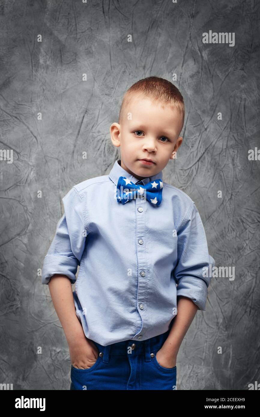 Portrait d'un joli petit garçon en Jean, chemise bleue et noeud papillon  sur un fond texturé gris en studio Photo Stock - Alamy