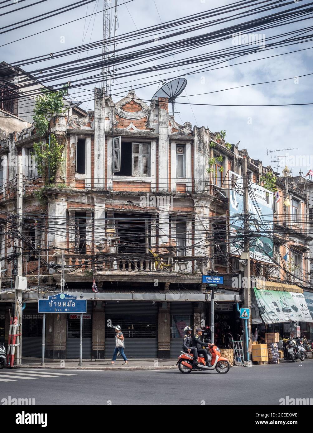Bangkok, Thaïlande, Asie du Sud-est - deux personnes à moto et une dame marchant devant l'ancien bâtiment. Câbles électriques compliqués. Banque D'Images