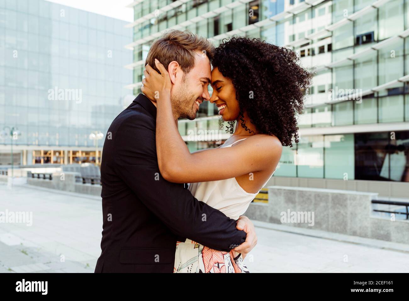 Vue latérale d'une jolie femme noire souriant et embrassant homme caucasien tout en se tenant sur la rue de la ville ensemble Banque D'Images