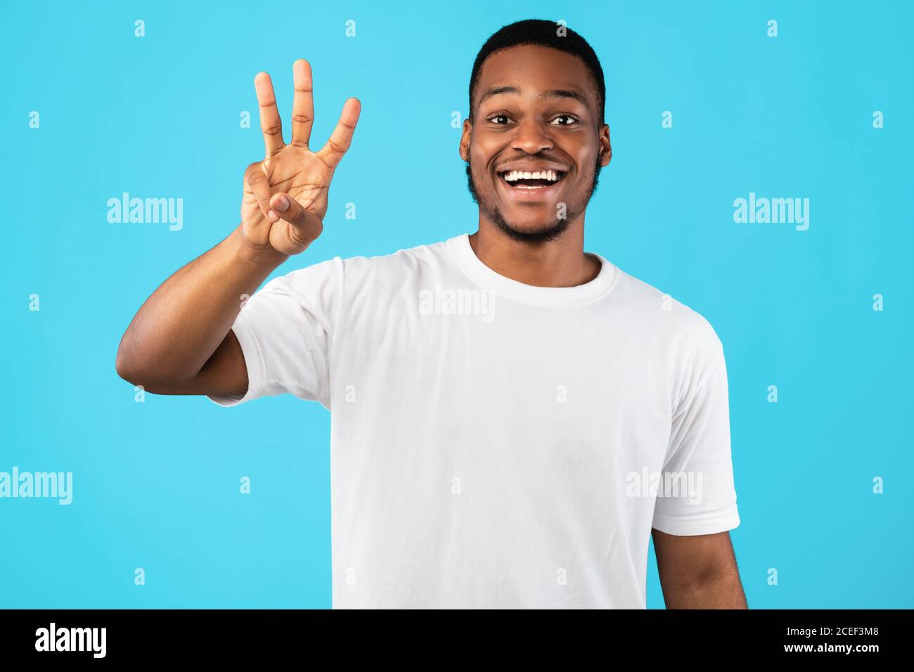 L'homme afro-américain montrant trois doigts comptant sur fond bleu Banque D'Images