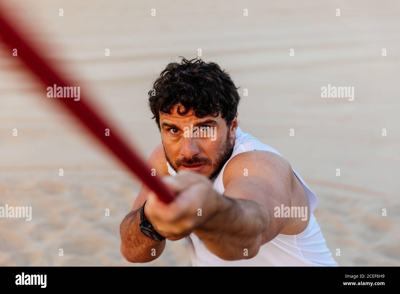 Beau barbu dans les vêtements de sport tirant la corde tout en faisant de l'exercice sur plage de sable Banque D'Images