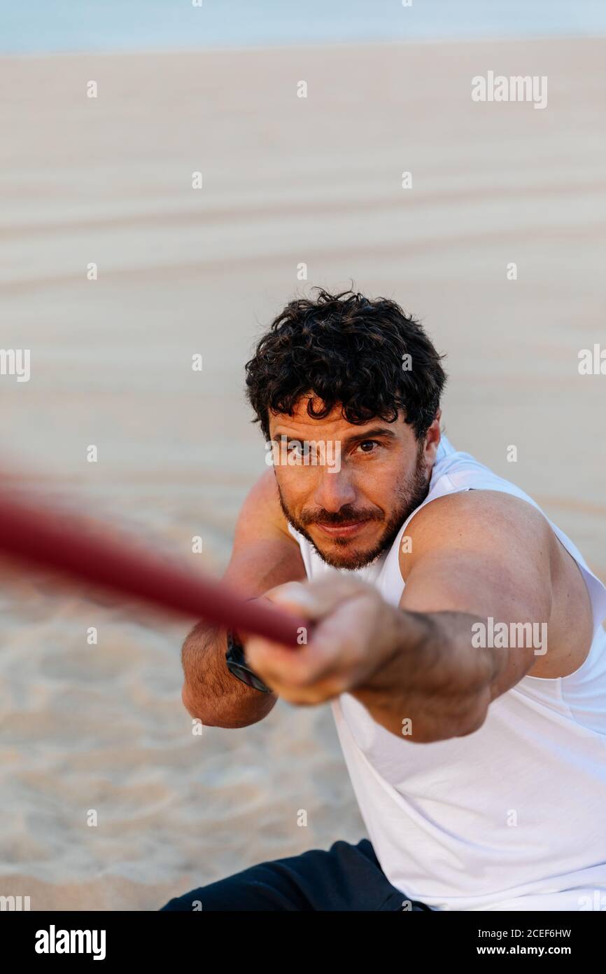 Beau barbu dans les vêtements de sport tirant la corde tout en faisant de l'exercice sur plage de sable Banque D'Images