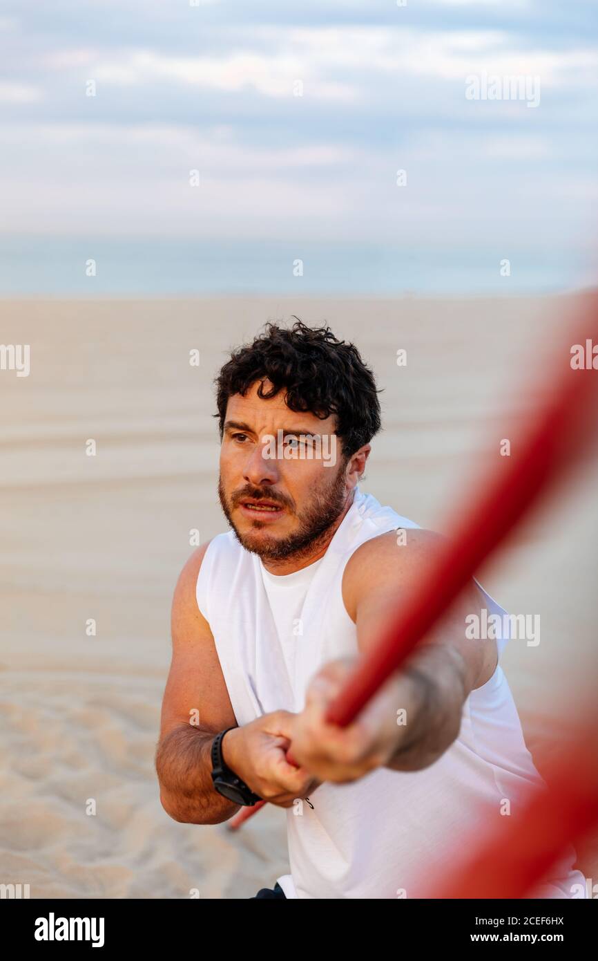 Beau barbu dans les vêtements de sport tirant la corde tout en faisant de l'exercice sur plage de sable Banque D'Images