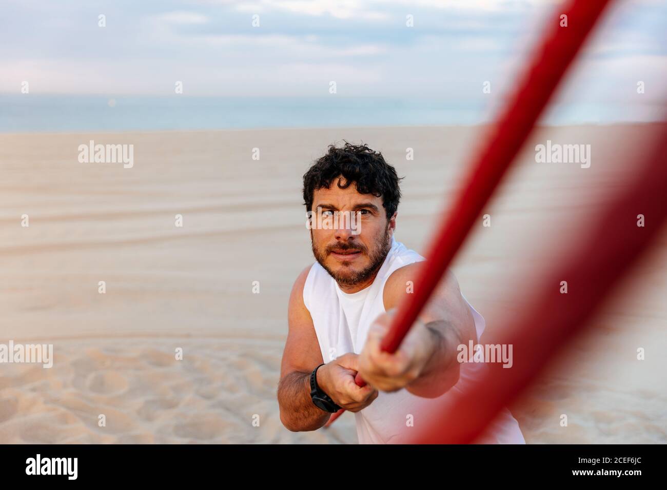 Beau barbu dans les vêtements de sport tirant la corde tout en faisant de l'exercice sur plage de sable Banque D'Images