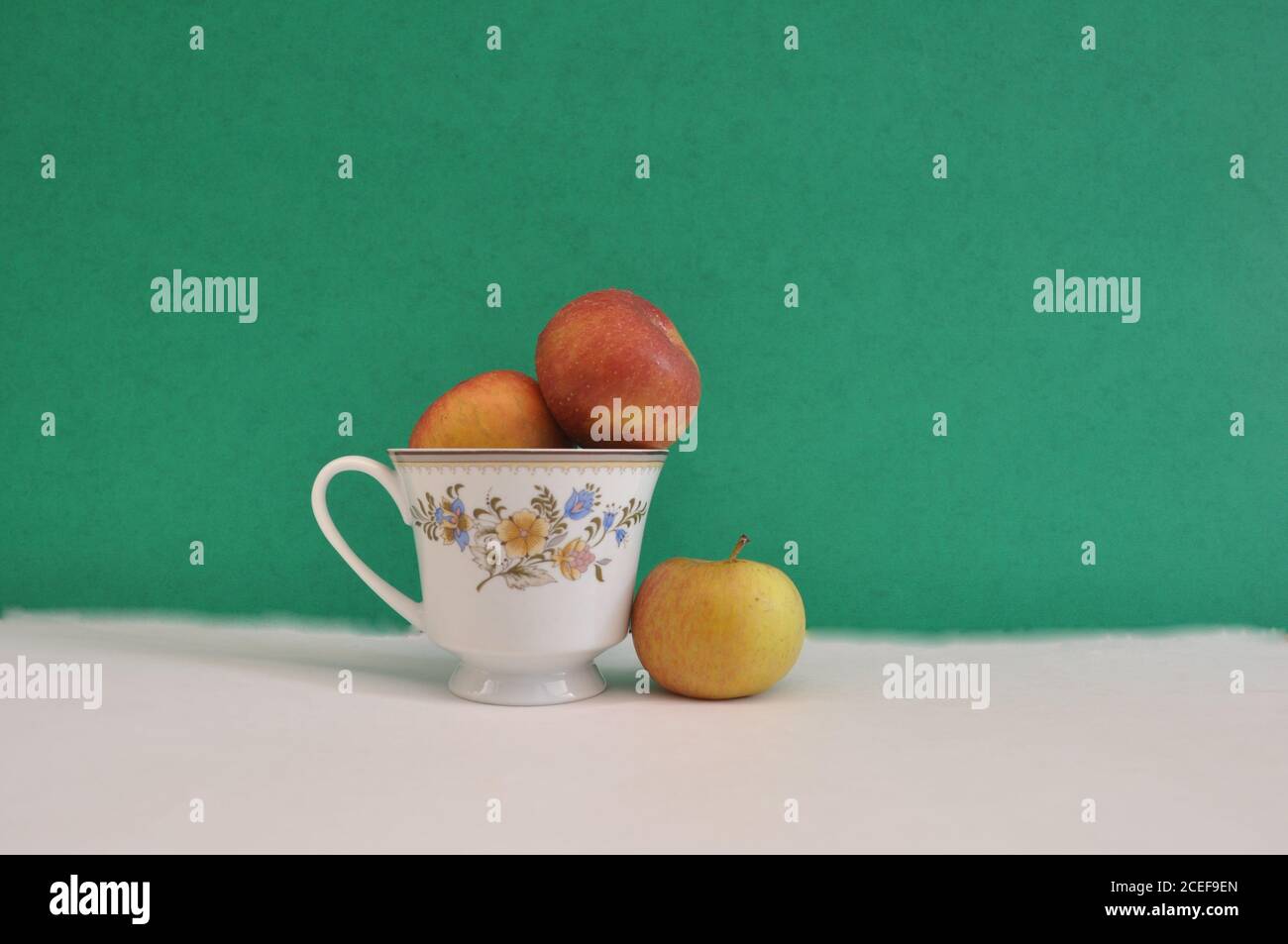 Tasse à café à motifs floraux, avec pommes fraîches à l'intérieur et à l'extérieur, photo conceptuelle de la séparation, de la ségrégation, sur fond blanc et vert Banque D'Images