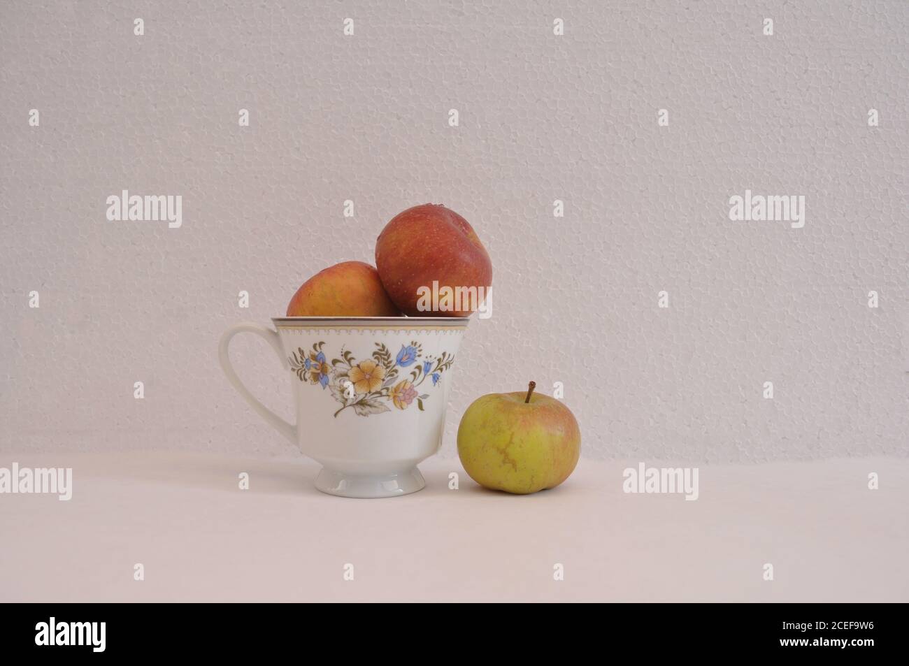 Tasse à café à motifs floraux, avec pommes fraîches à l'intérieur et à l'extérieur, photo conceptuelle de la séparation, de la ségrégation, sur fond blanc et blanc Banque D'Images