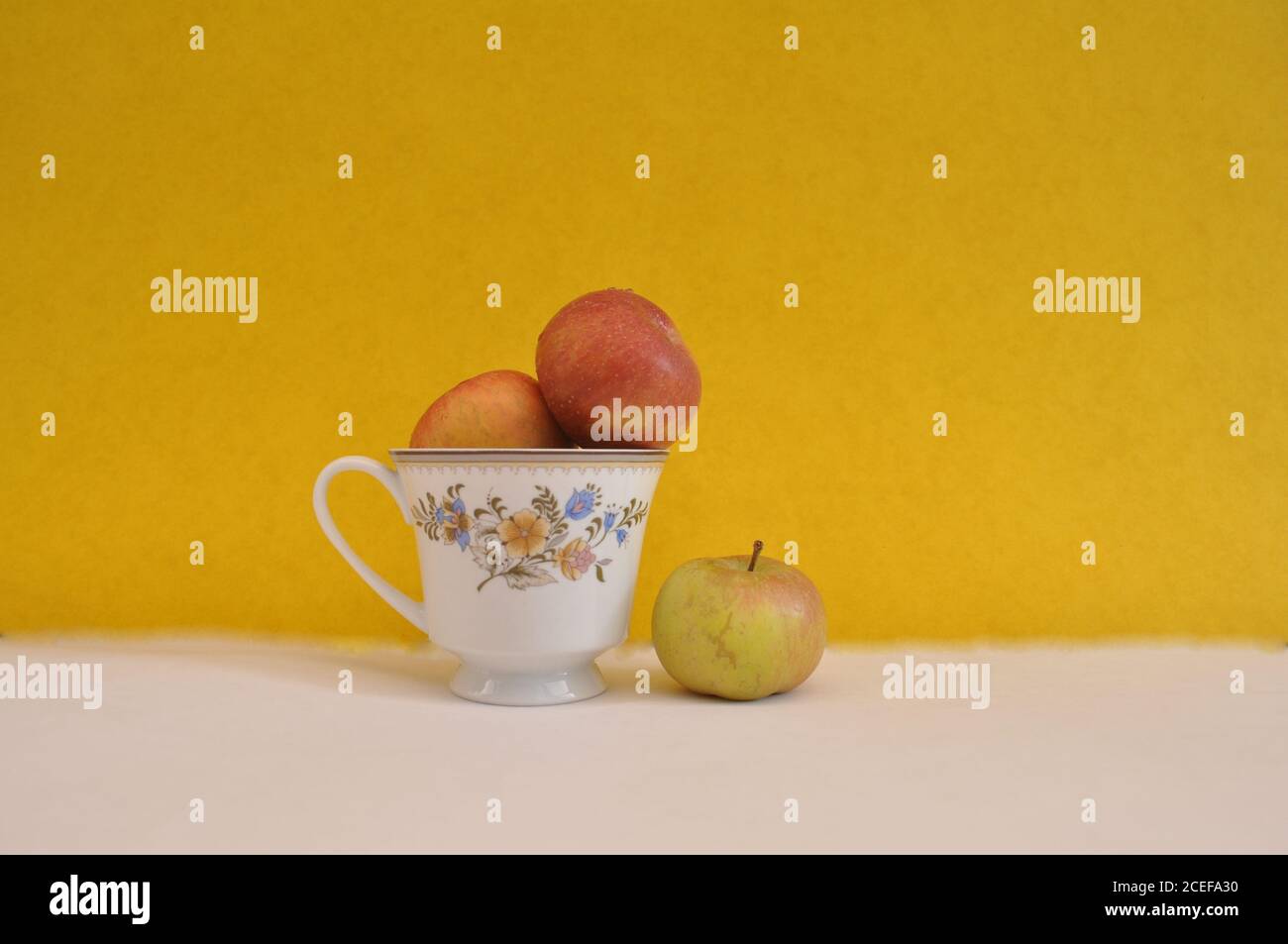 Tasse à café à motifs floraux, avec pommes fraîches à l'intérieur et à l'extérieur, photo conceptuelle de la séparation, de la ségrégation, sur fond blanc et jaune Banque D'Images