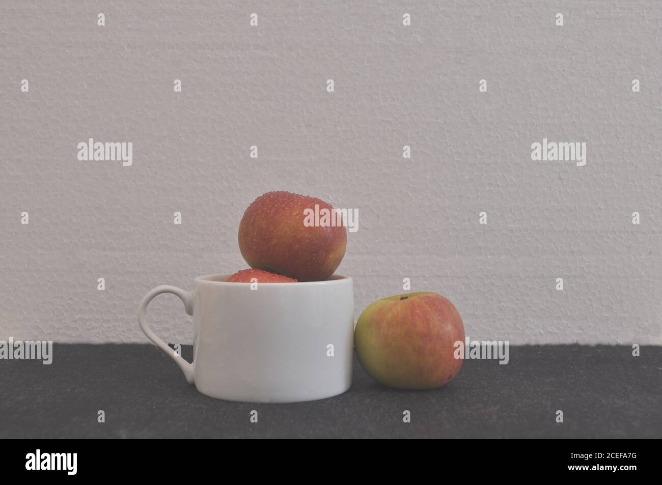 Pommes. En tasse de café en céramique blanche, avec une pomme isolée donnant le concept de séparation, de discrimination, de photo conceptuelle, fond blanc, Braz Banque D'Images