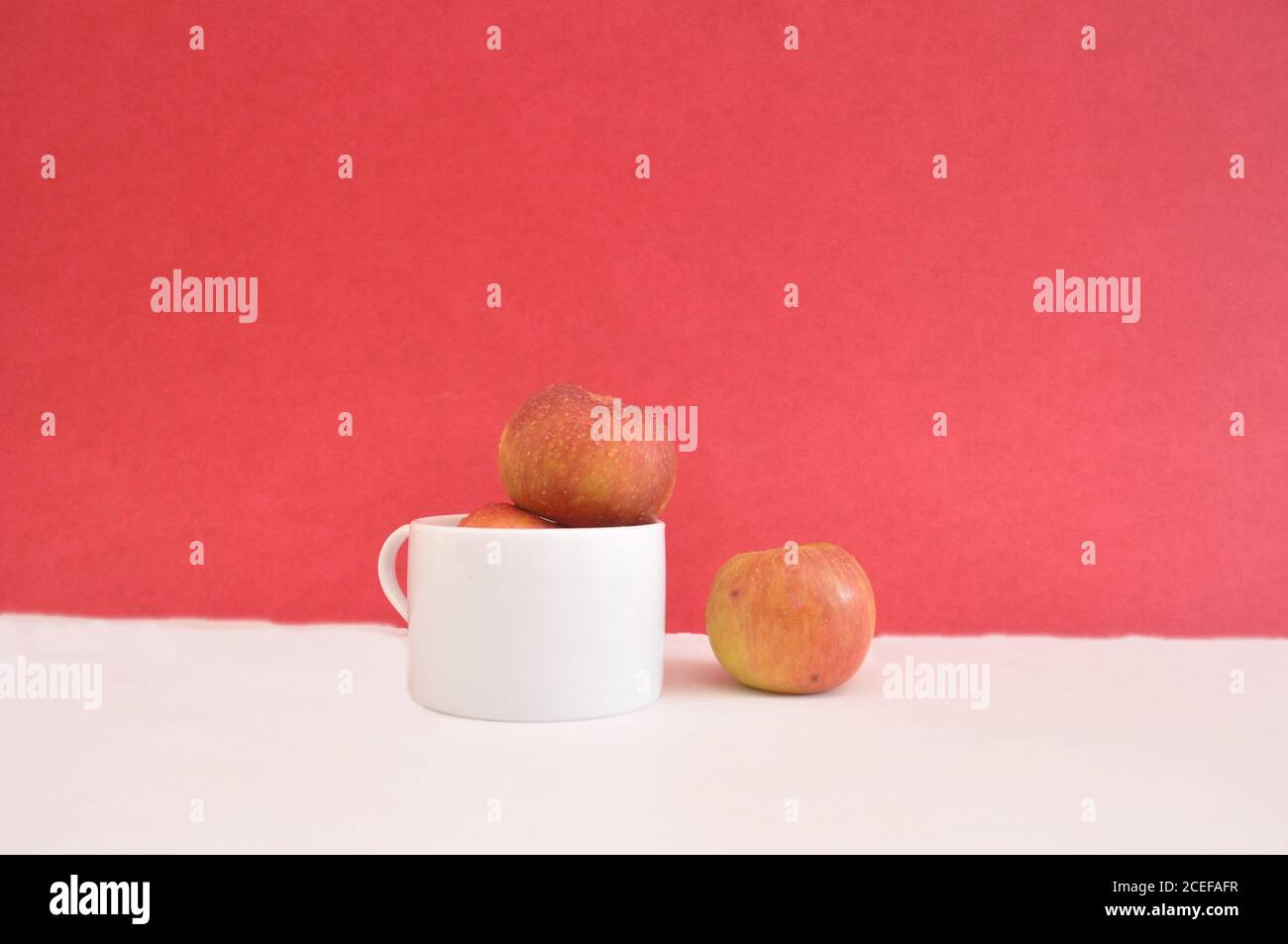 Pommes dans une tasse blanche avec une pomme isolée concept de séparation d'arrière-plan rouge Banque D'Images