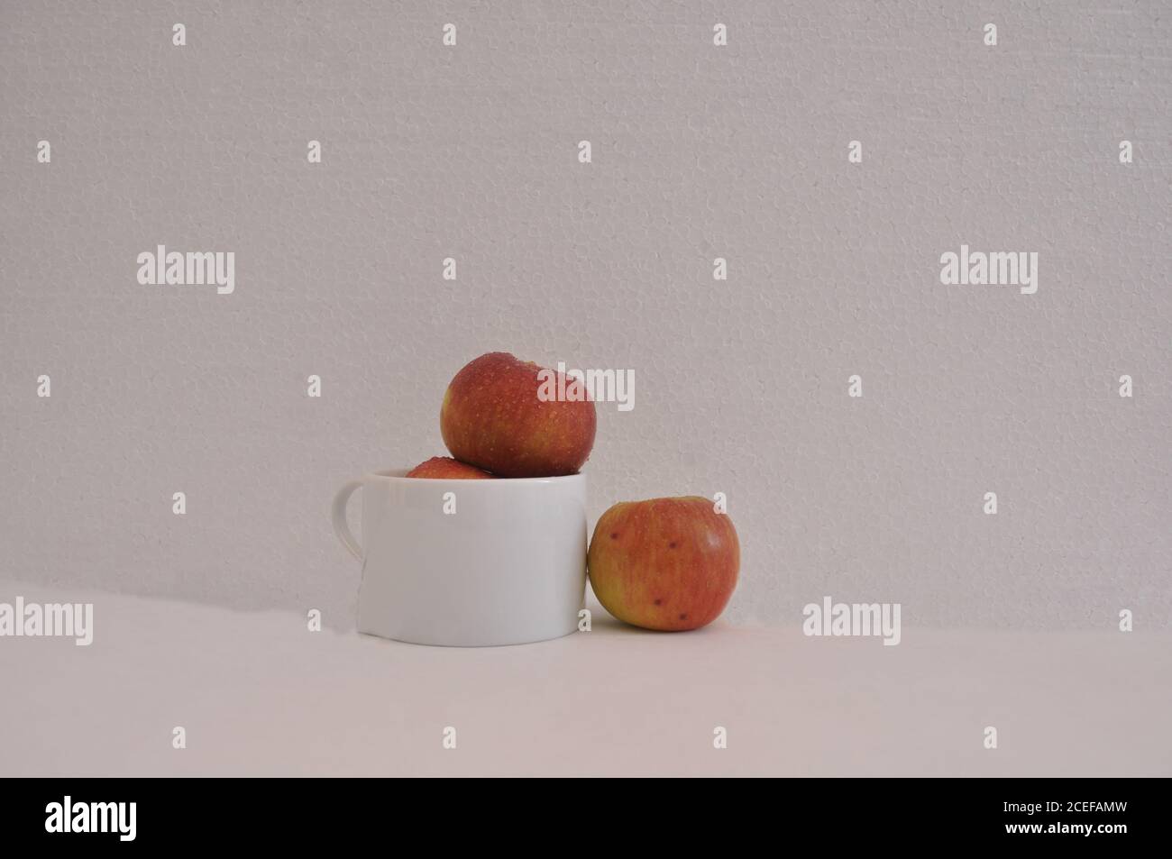 Pommes rouges, dans une tasse de café en céramique blanche, pleine, avec une pomme sur le côté, photo conceptuelle, fond blanc, Brésil, Amérique du Sud Banque D'Images