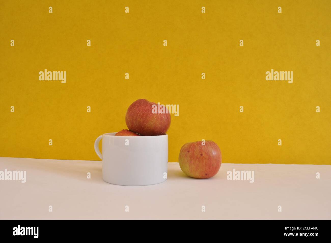 Pommes dans une tasse blanche avec une pomme isolée concept de séparation d'arrière-plan jaune Banque D'Images