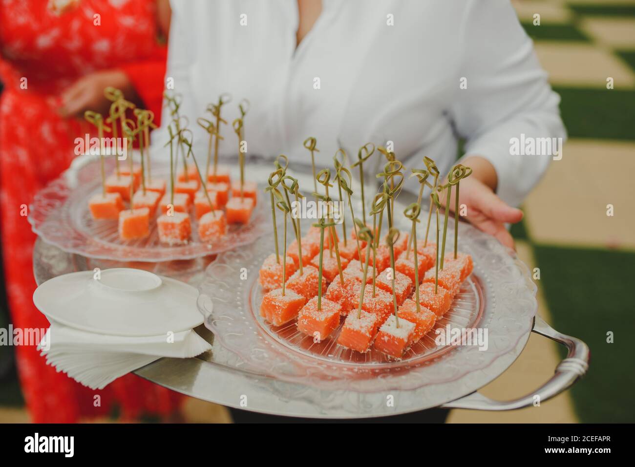 femme méconnue en uniforme de serveuse portant un plateau métallique avec du yummy canapés de pastèque pendant le banquet de mariage Banque D'Images