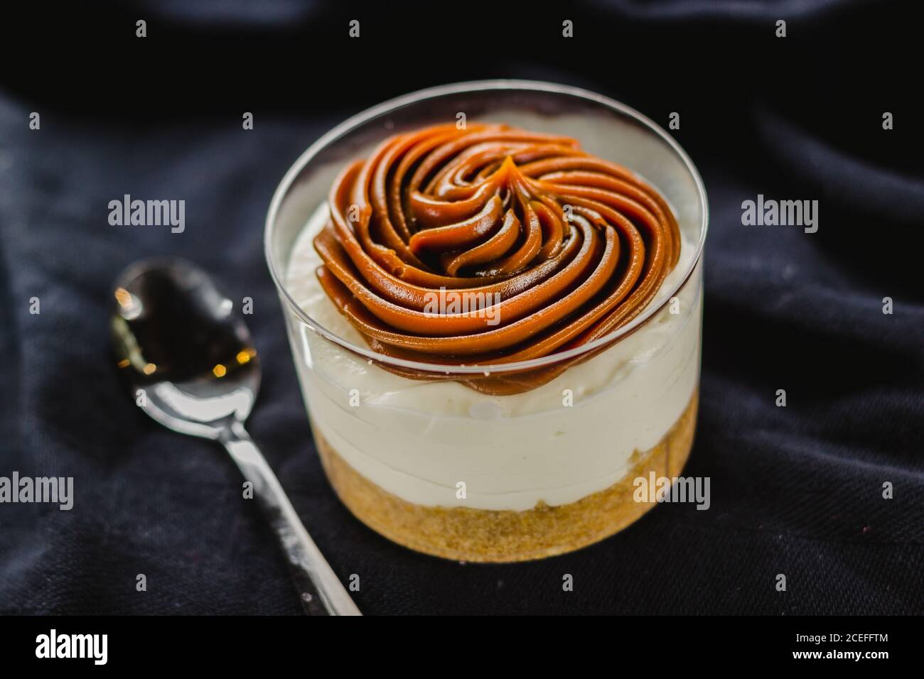 Gros plan d'un dessert crémeux composé d'une tasse et recouvert d'une délicieuse crème servie sur du noir avec une cuillère. Banque D'Images