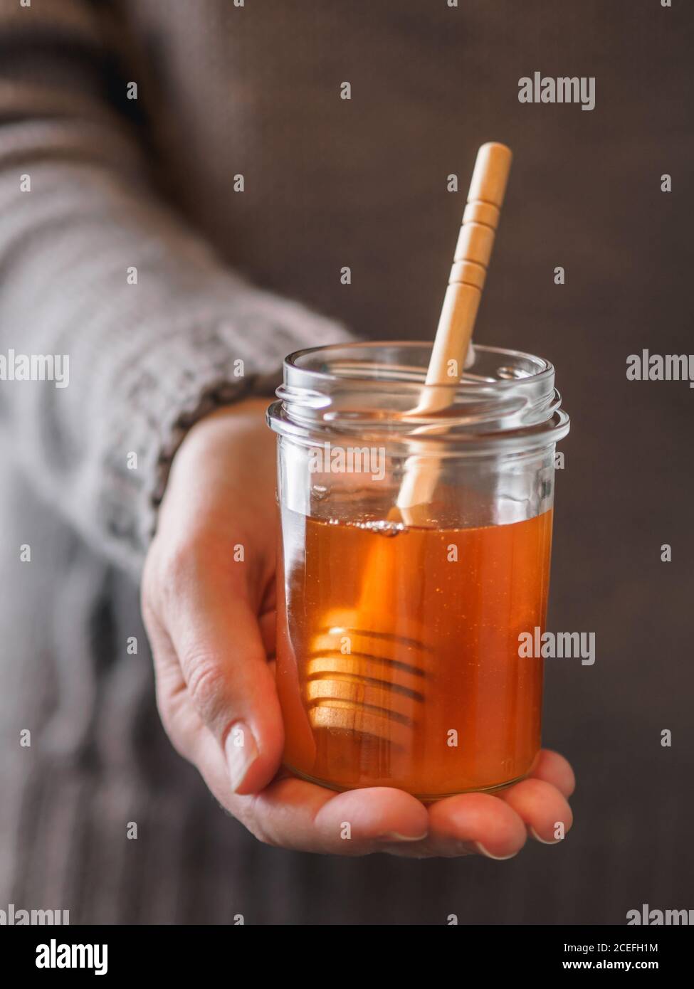 Gros plan de la main d'une femme anonyme tenant un petit pot de miel frais avec une cuillère Banque D'Images