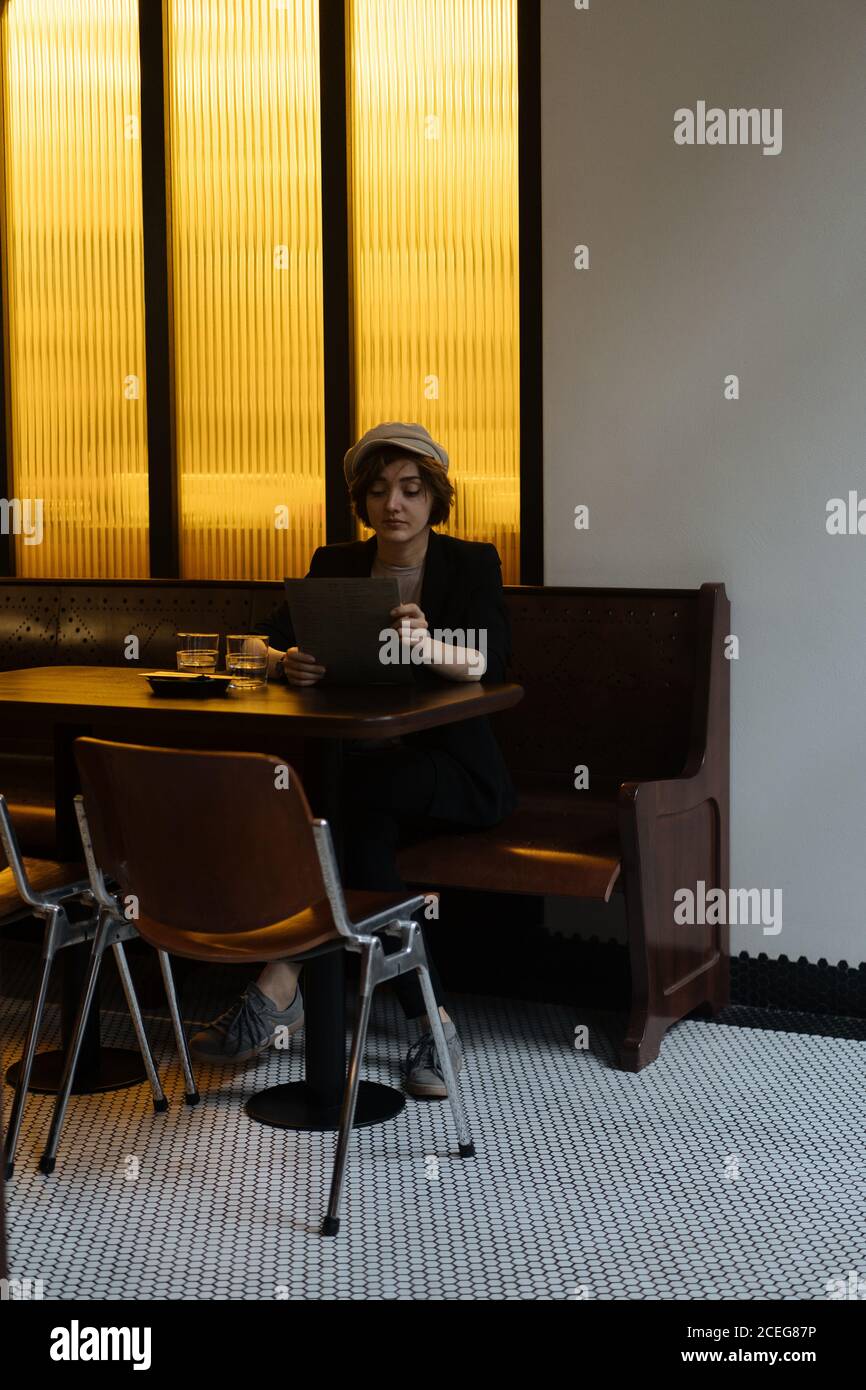 Jeune jolie femme au Cap assise seule à table dans un restaurant moderne et lisant le menu Banque D'Images