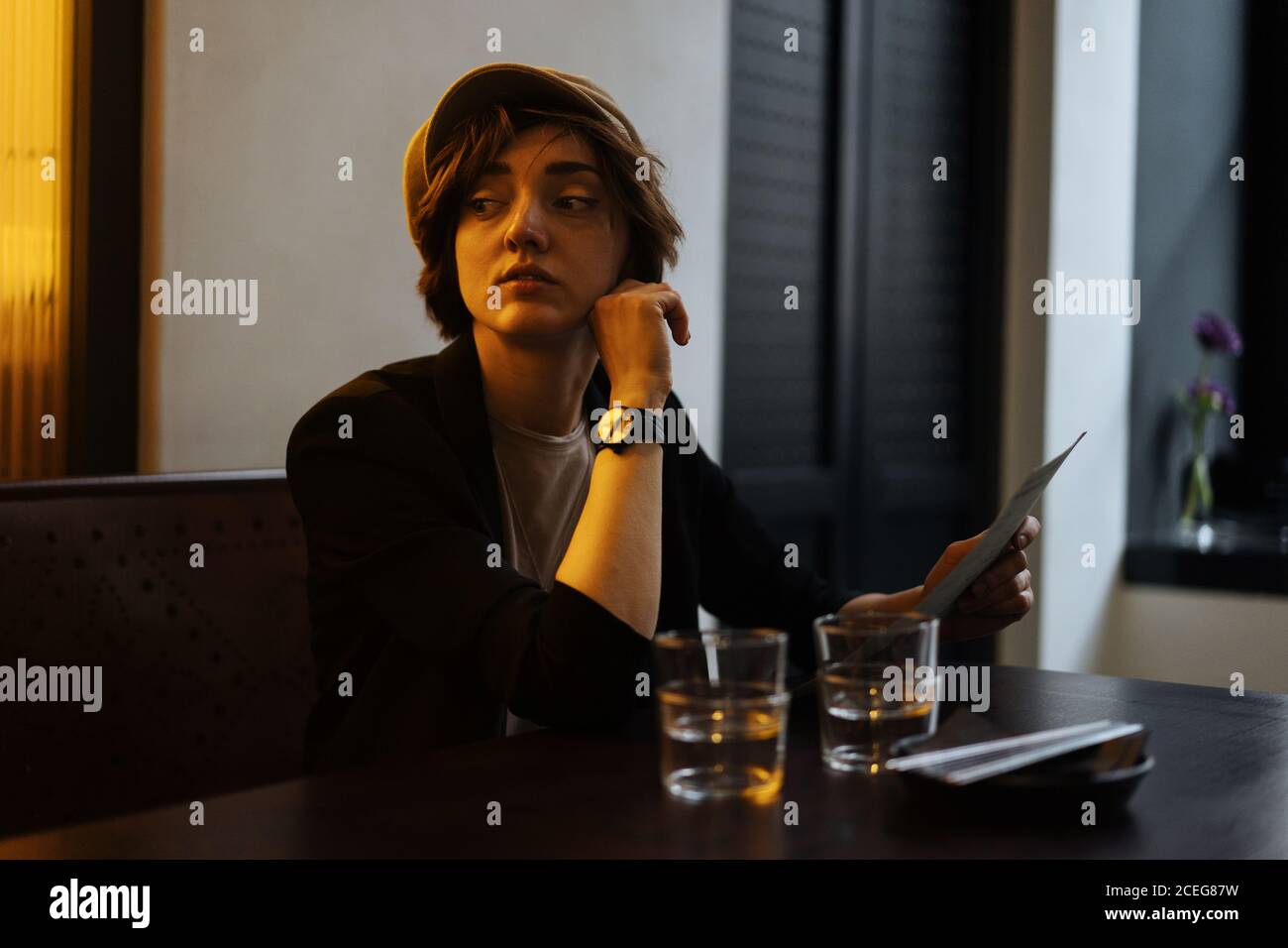 Jeune jolie femme au Cap assise seule à table dans un restaurant moderne et lisant le menu Banque D'Images
