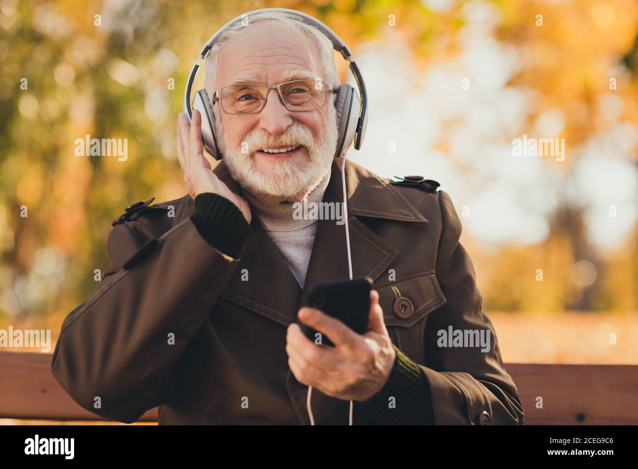 Photo de gai retraité vieux gris poil grand-père se sentir jeune rue assis banc écouter la chanson des jeunes musique grands écouteurs suivre tendances des petits-enfants Banque D'Images
