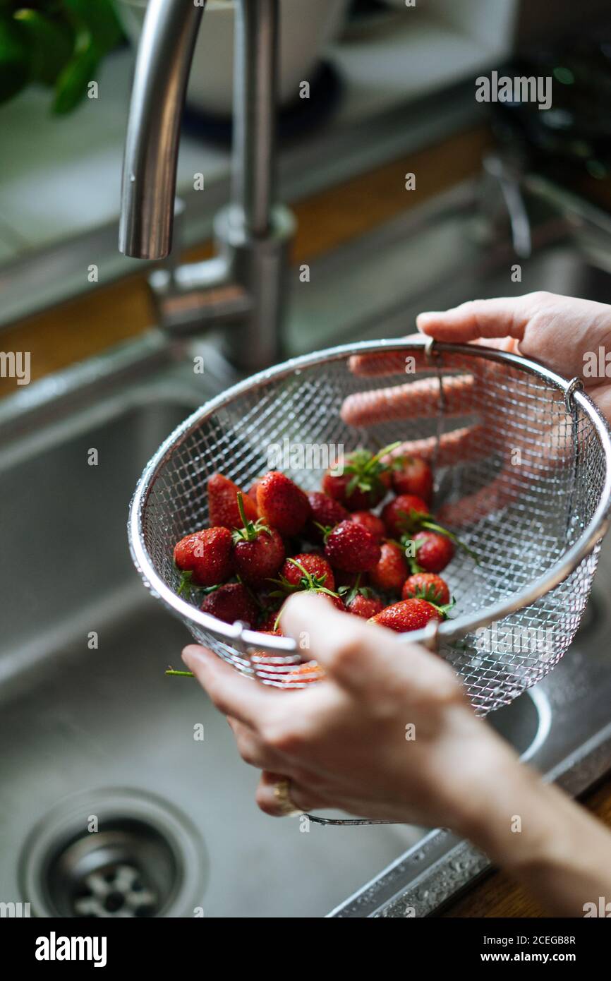 Rognez les mains des femmes en tenant la crépine métallique avec des fraises fraîches et brillantes sous l'évier, tapez sur le comptoir en bois par le dessus Banque D'Images