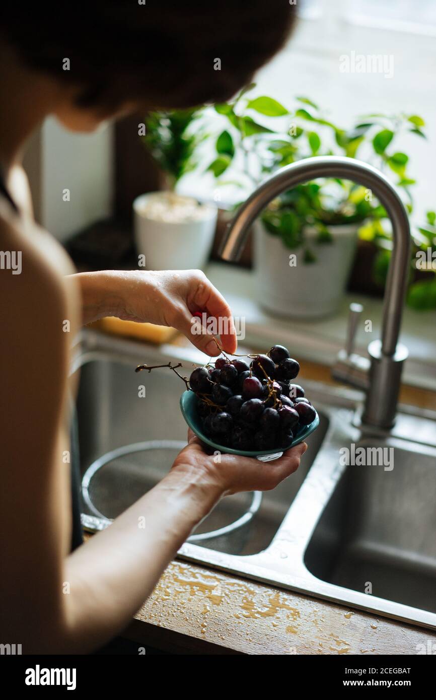 Rognez les mains des femmes en tenant la crépine métallique avec des fraises à raisins brillants sous l'évier, tapez sur le comptoir en bois par le dessus Banque D'Images