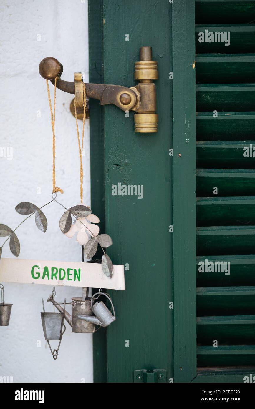 Vue rapprochée de l'ancienne porte rustique en bois vert avec usé serrure en bronze et magnifique panneau de jardin en métal avec arrosoir et des figurines de seau accrochées à la paroi en plâtres blanche Banque D'Images