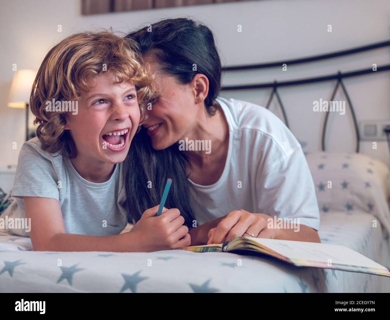 Belle femme et enfant mignon couché sur un lit confortable et coloriage des photos dans le carnet ensemble. Banque D'Images