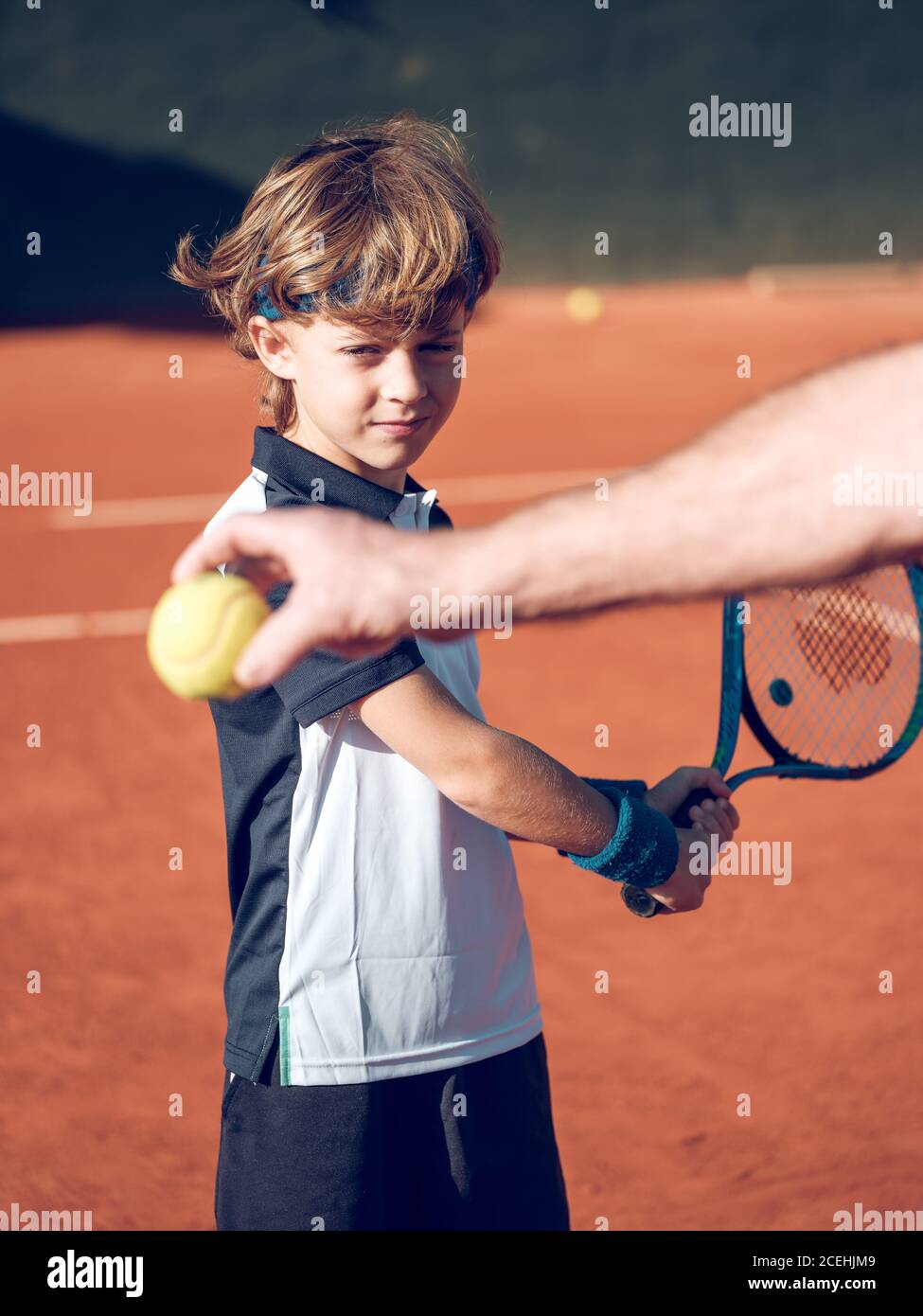 Petite main de l'homme âgé tenant le ballon de tennis et peu enfant dans le  congé bleu essayant de frapper le ballon avec le tennis raquette sur le  terrain par temps ensoleillé