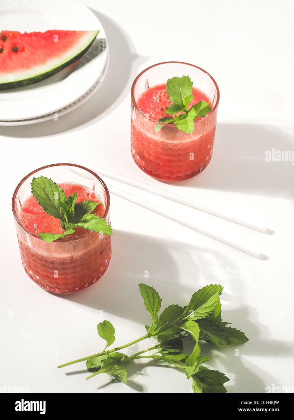 Deux verres de smoothie frais rouge melon d'eau avec des pailles à boire à la menthe et au papier sur une table blanche. Prise de vue en hauteur avec espace de copie. Minimalisme. Banque D'Images