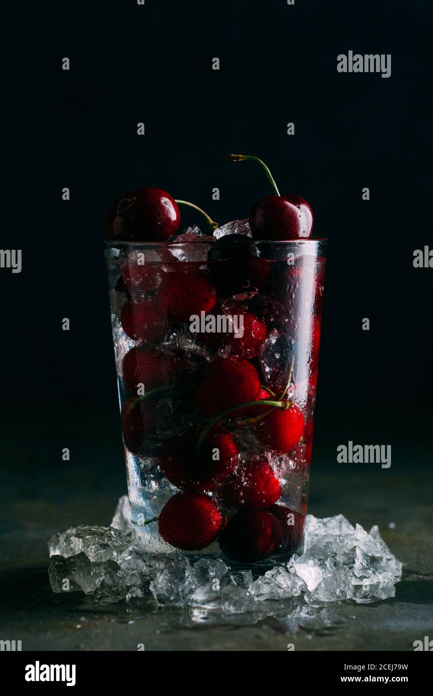 Cerises dans un verre avec de la glace sur fond sombre Banque D'Images