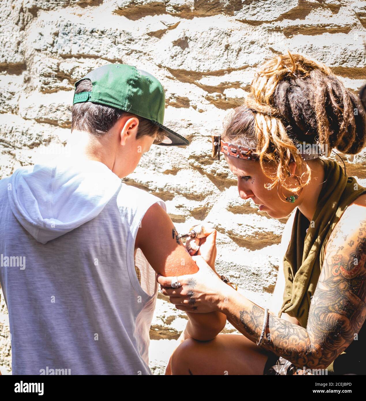 MARCHÉ MÉDIÉVAL - PUEBLA DE SANABRIA - ZAMORA - ESPAGNE - AGOUST 13, 2017: Femme adulte assise et dessinant un tatouage instantané avec de la peinture au jeune garçon au mur de pierre Banque D'Images