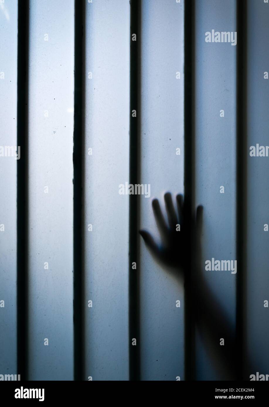 Silhouette de la main rognée touchant le mur bleu avec des barres métalliques Banque D'Images