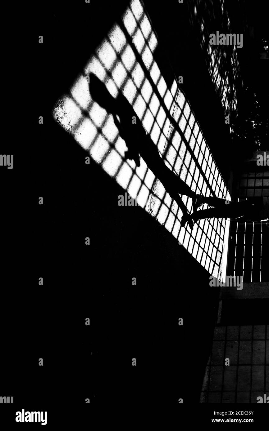 Silhouette d'une personne méconnaissable qui marche au niveau de la grille dans une pièce verrouillée Banque D'Images