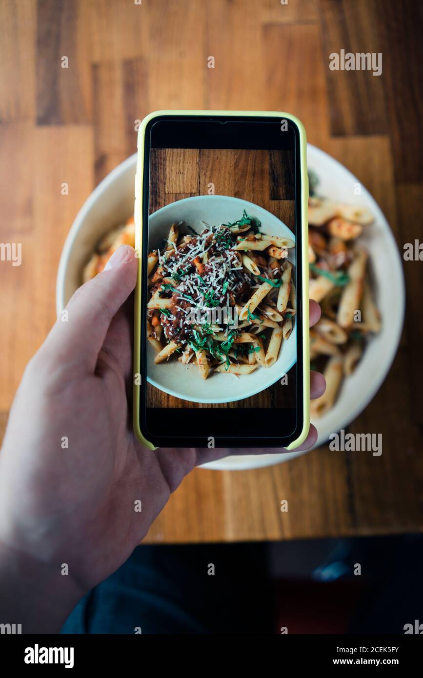 Rognez à la main en prenant une photo de bolognaise macaroni avec de la sauce à la viande avec tomate et fromage Banque D'Images