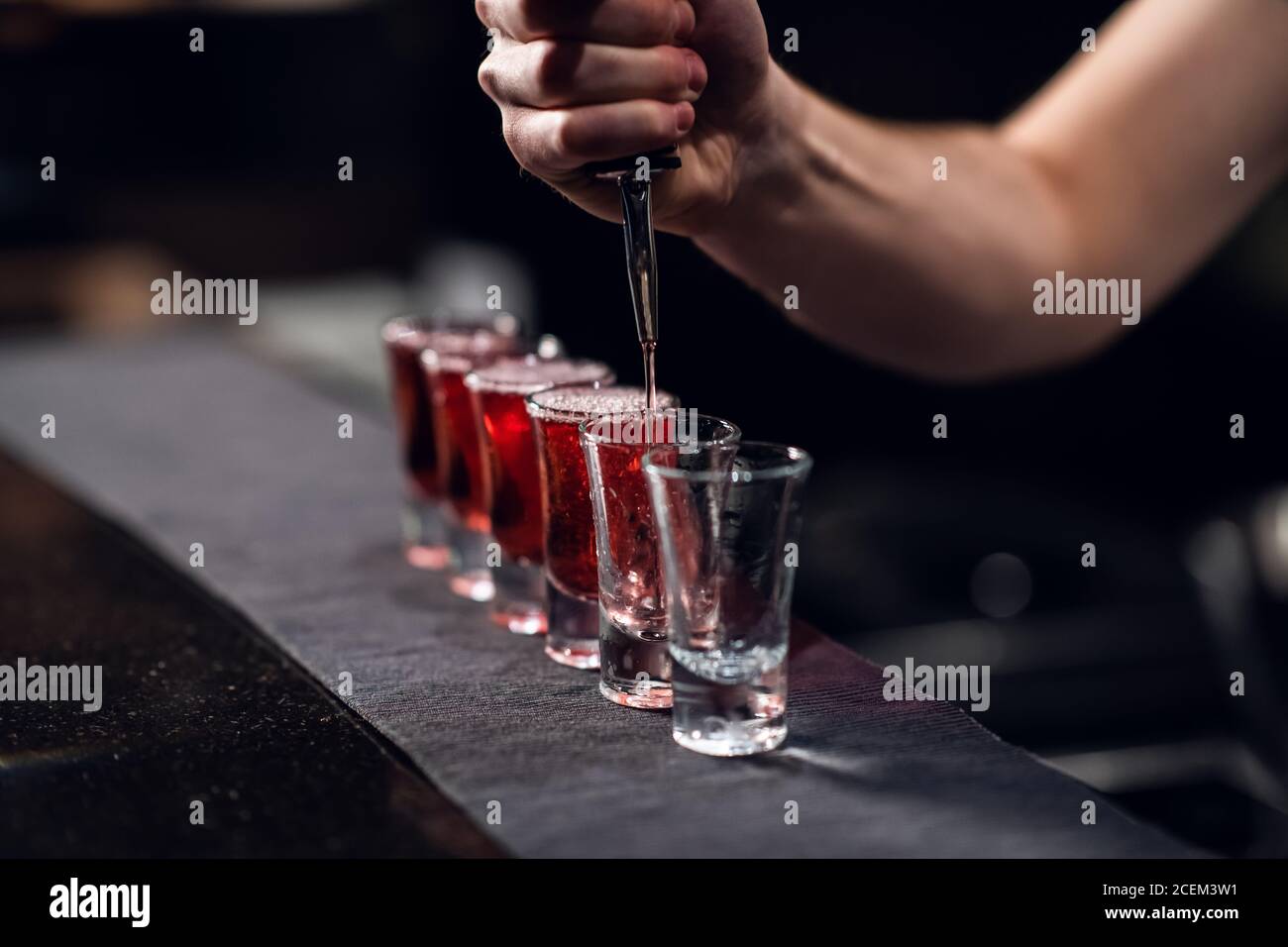 le barman verse de l'alcool rouge dans des coups de feu sur le bar, le spectacle du barman. Banque D'Images