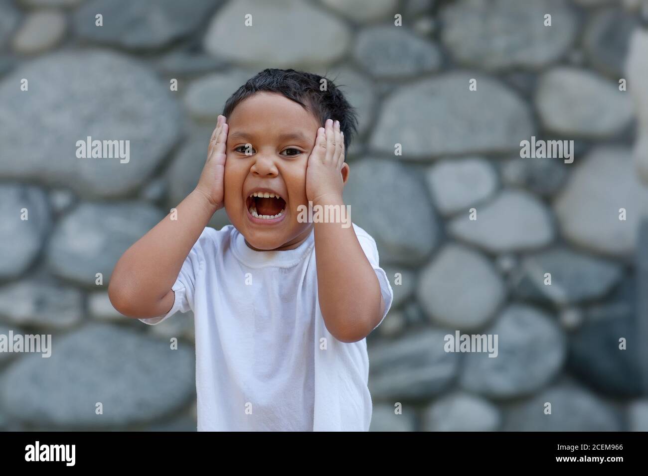 Jeune latino garçon tenant sa tête avec les deux mains tout en riant fort exprimant la joie. Banque D'Images