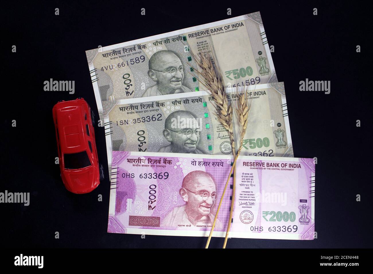 Nouvelles devises indiennes. 500, et 2000 roupies notes avec grains de blé et voiture de jouet de couleur rouge. Monnaie indienne isolée sur fond noir. Banque D'Images