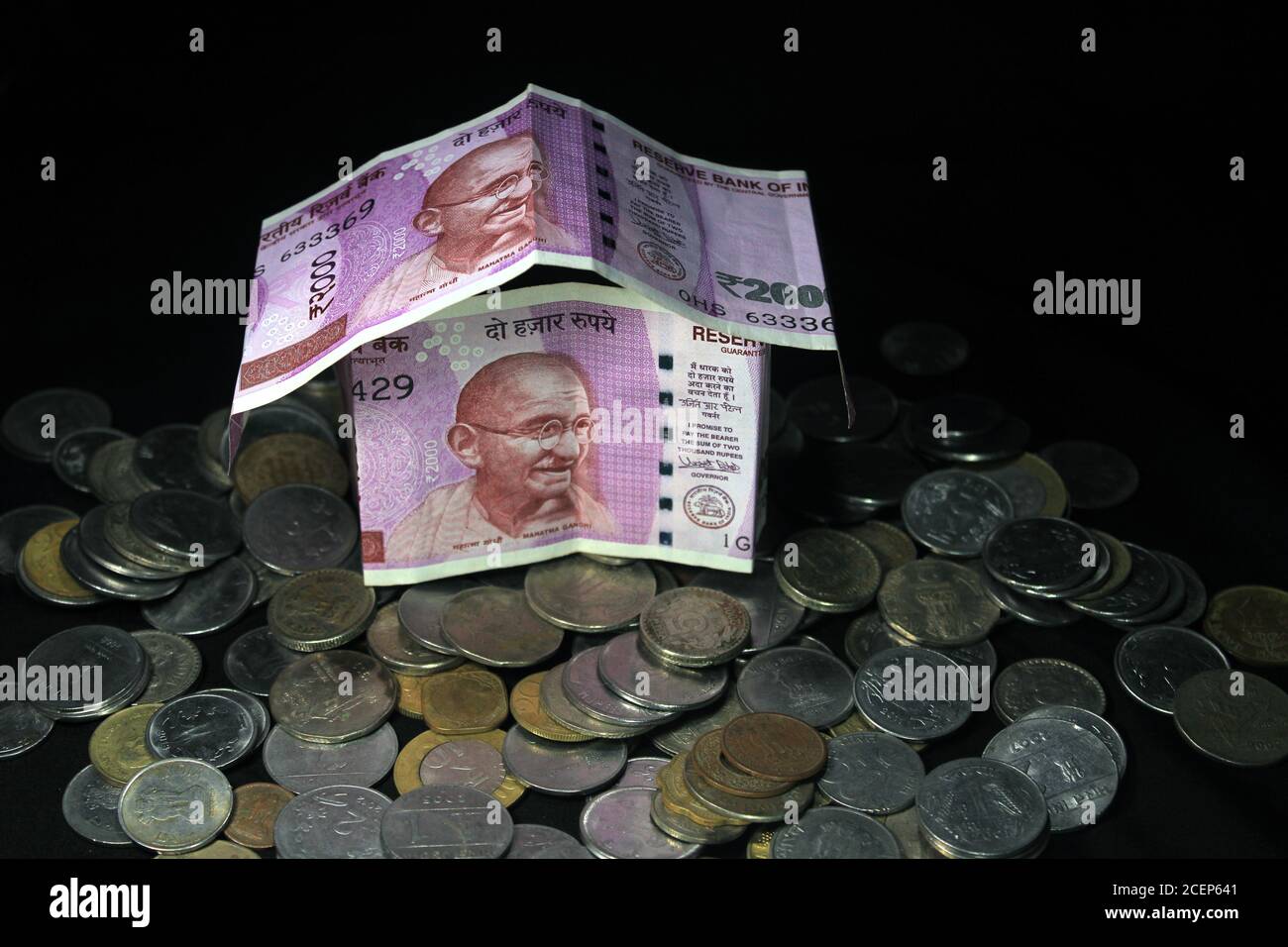 Concept de billets de banque de roupie indienne pliés en forme d'une maison simple sur fond noir. Nouvelle monnaie indienne. note de 2000 roupies avec pièces. Banque D'Images