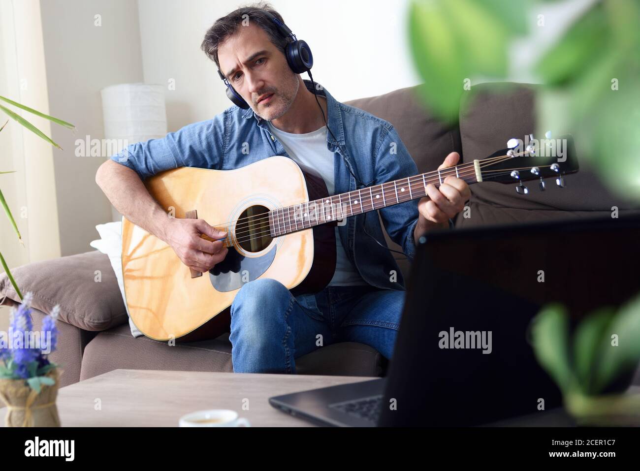 Homme écoutant de la musique avec des écouteurs et jouant de la guitare regarder un ordinateur portable en même temps dans le séjour à la maison Banque D'Images